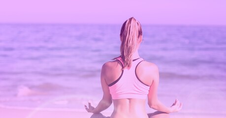 Rear view of caucasian fit woman practicing yoga over seaside background