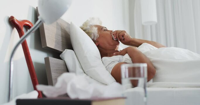 Sick african american senior woman holding tissue coughing while lying on the bed at home