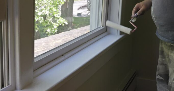 Worker painting using paint roller on layer white color a window frame trim at home renovation