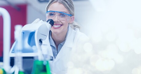 Composition of smiling female lab technicians using microscope, with white bokeh copy space to right