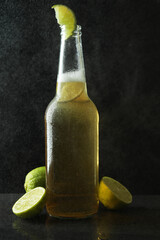 Wet bottle of beer with lime against dark background
