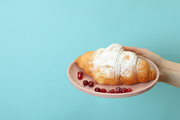 Female hand holds plate with croissant on blue background