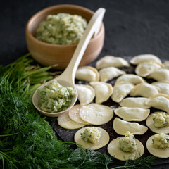 Dumplings with potatoes and dill. Product for eating or freezing, cooking process. Raw dough stuffed with mashed potatoes and dill on black background of kitchen table. Convenience Food concept.