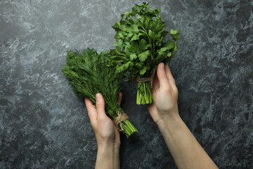 Female hands hold dill and parsley on black smokey table