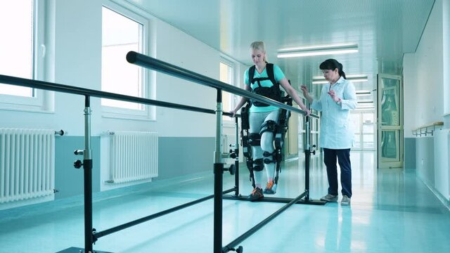 Doctor is helping a young woman to walk in the exoskeleton