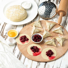 Raw Dough stuffed with cherry. Convenience Food Cooking process. Flat lay. Sweet Dumplings, Ingredients and kitchen utensils to making Food at wooden cutting board.
