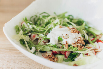Summer vegetable salad with fresh cabbage radishes, walnuts, sour cream on a white plate