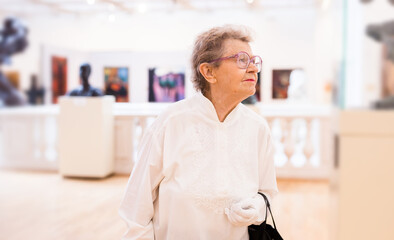 mature woman  examines paintings in an exhibition in hall of an art museum