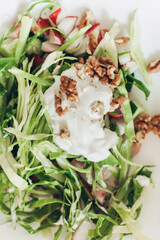 Summer vegetable salad chopped with fresh cabbage radishes, walnuts, sour cream on a white background 