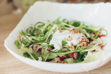 Summer vegetable salad with fresh cabbage radishes, walnuts, sour cream on a white plate