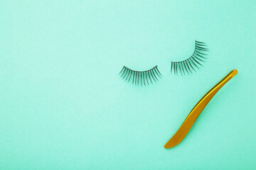 Set of false eyelashes extencions on mint background with tweezer. Minimalism