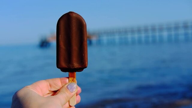 chocolate ice cream on stick in hands on the background of the sea in women's hand