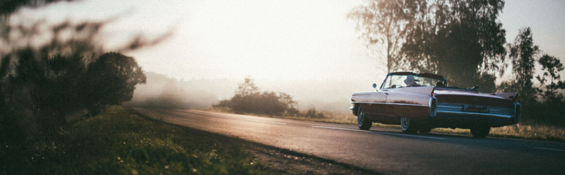 Fototapeta A retro car drives along the road at dawn. The convertible drives off into the distance on a deserted road