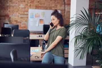 Obraz premium Young woman, architect or interior designer looking away while talking on the phone, standing in modern green office and discussing new project