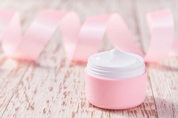 Natural face or body cream and pink silk ribbon on a white background.