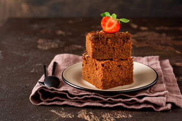 Stack of pieces or bar of chocolate cake brownie with strawberries and pistachio nuts on the black background, selective focus image