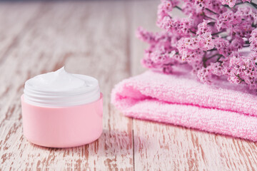 Natural face skincare product  in pink plastic jar with towel on white table. Plastic pink jar of sensitive skin cream on a wooden table.