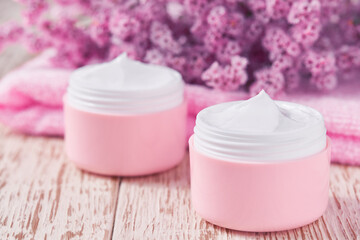 Natural face cream or lotion, organic cosmetic product to moisturize the skin with a towel and flowers on the background. Pink series  cosmetic.