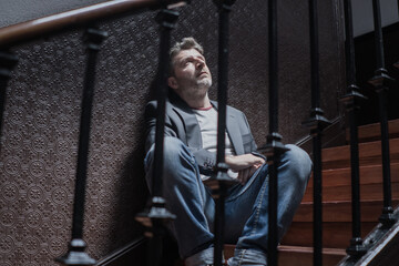 Fototapeta na wymiar unemployment and divorce - dramatic lifestyle portrait of sad and depressed man on his 40s sitting indoors on staircase thoughtful and worried suffering depression problem