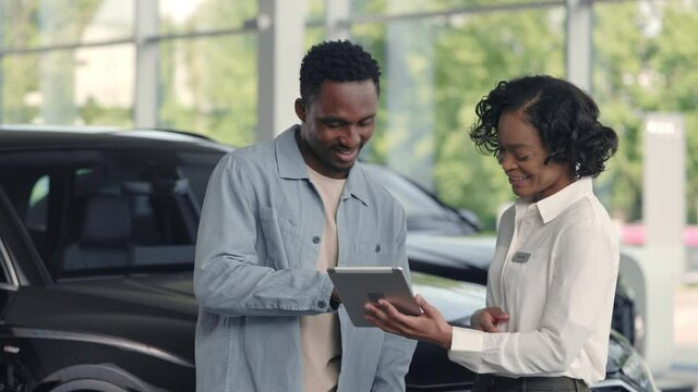 Female car dealer with tablet shaking hands with male client