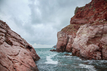 Fototapeta na wymiar Seascape with red coastal rocks on a cloudy day.
