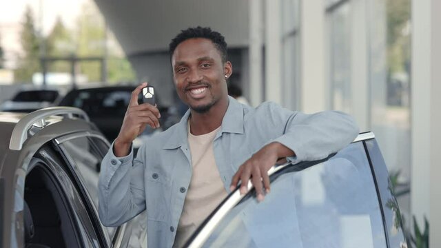 Smiling african man posing near car with keys in hands