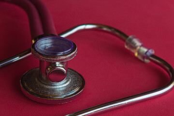 Red stethoscope, equipment to examine respiration and heartbeat. Red background.