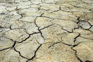 Dried brown clay surface covered with cracks. A bright, sunny day. Harsh shadows. Angle view, background.
