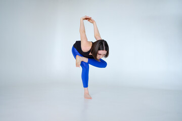 Portrait of sporty woman doing Kapotasana or standing Pigeon Pose. Attractive young woman training yoga on white background isolated on cyclorama.