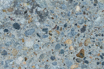 Flat surface of gray concrete. The material has inclusions of brown and brown rubble. The surface is rough and rough. Texture close-up view.