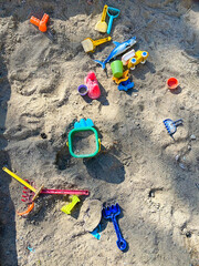 Colourful toys in a sandbox in sunlight. Rakes, spades and plastic animals.