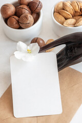 Business card with space for design and small fresh flower on hand shaped holder near nuts bowls on white table extreme closeup