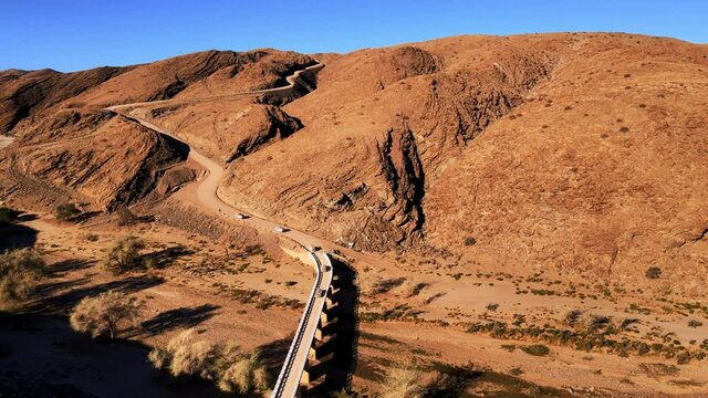 Srone shot of group of suv on desert serpentine road. Tourists having halt during expidition in african national park. Travellers exploring beauty of nature around cliffs and canyon shot by drone.