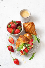 Tasty breakfast wholegrain croissant sandwich with strawberries, arugula and  camembert cheese.