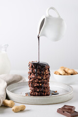 Chocolate topping pouring from a levitating milk jug onto chocolate cookies with peanuts. Food levitation.