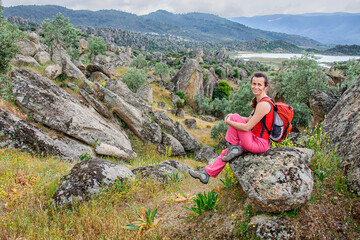 A girl with a backpack on her back sits on a huge boulder in a dolly among the scattered stones. Turkey