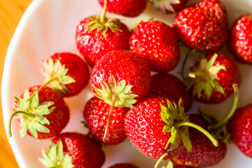 Ripe fresh strawberries on white plate with long shadow, close up.