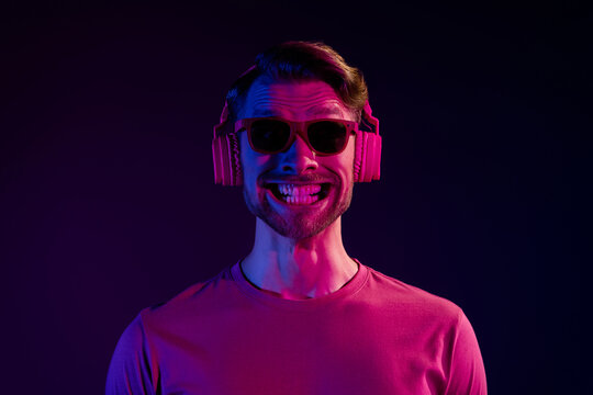 Portrait of attractive cheerful funny guy listening bass grinning teeth good mood isolated over dark neon violet color background