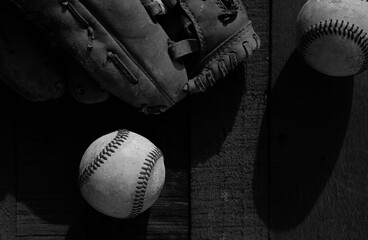 Baseball dark flat lay with grunge sport equipment, top view of balls and glove on wood background in black and white.