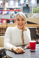 Vertical shot of a blonde Hispanic female smileing sit in a cafe