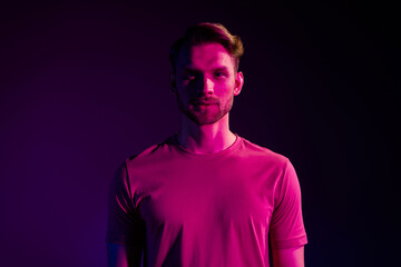 Portrait of attractive serious content guy wearing t-shirt isolated over dark neon light violet...