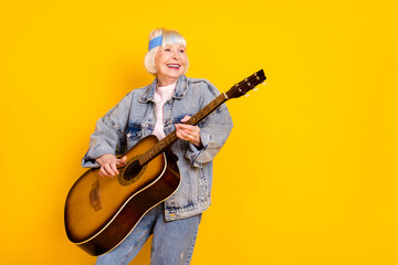 Fototapeta premium Photo portrait of elder woman playing acoustic guitar on festival feeling young isolated vivid yellow color background