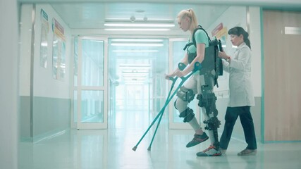 Doctor is helping a woman to walk along the hospital in exoskeleton