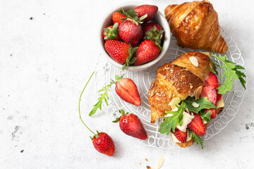 Tasty breakfast wholegrain croissant sandwich with strawberries, arugula and  camembert cheese.