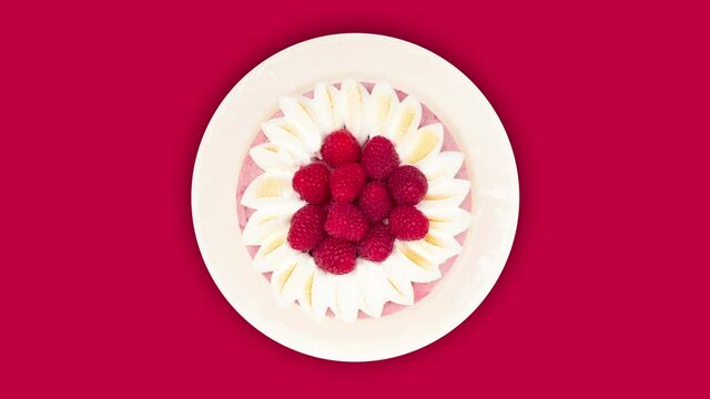 Rotating raspberry yogurt cake on white plate against red background, top view, seamless loop in 4k