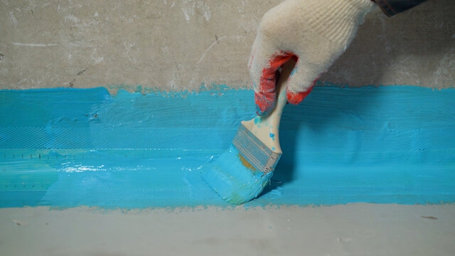A worker is applying waterproofing paint to the floor in the bathroom. The process of applying waterproofing in the bathroom.