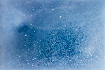 Aerial view of abstract patterns formed by small glass-like cracks within a blue and white frozen ice sheet
