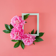 fresh pink peony with green leaves and frame on pink pastel background with copy space. minimal tropical summer flat lay with copy space. minimal garden background.