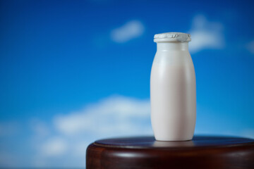 Natural liquid yogurt with probiotics in small plastic bottles on wooden table on background of green trees.