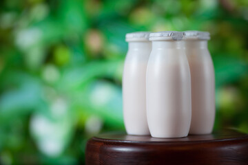 Natural liquid yogurt with probiotics in small plastic bottles on wooden table on background of green trees.